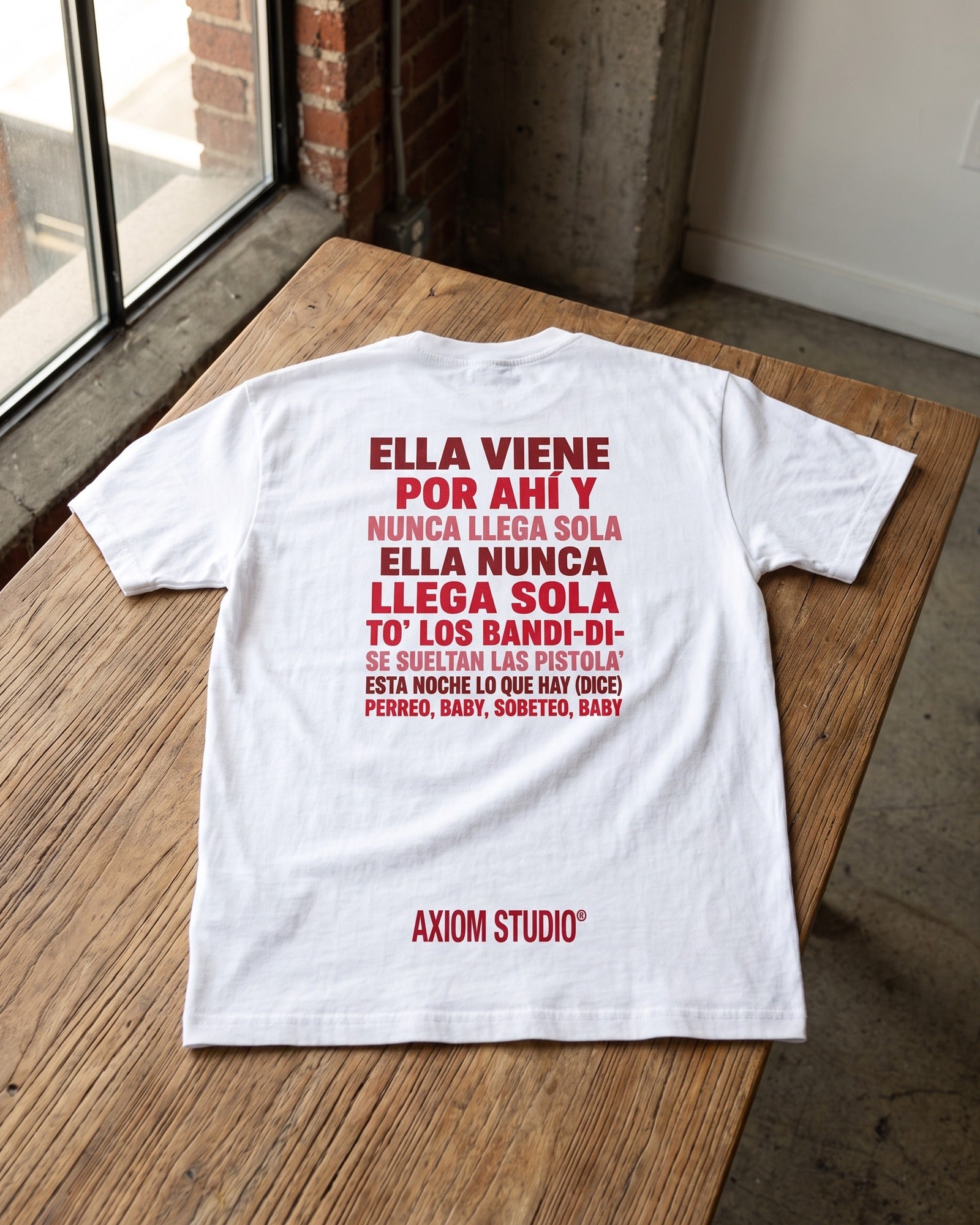 Camiseta SOBETEO SPIDER blanca doblada sobre una mesa de madera, vista por la espalda